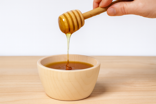 Drewniana miska z miodem – ręka z nabierakiem delikatnie polewa złocisty miód do miski z naturalnego drewna bukowego – Chłopcy z Rancza.