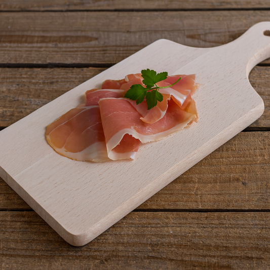 Drewniana deska do krojenia z kilkoma plastrami szynki parmeńskiej ozdobionymi gałązką pietruszki, na tle rustykalnego stołu – Chłopcy z Rancza / Ranch Boys.