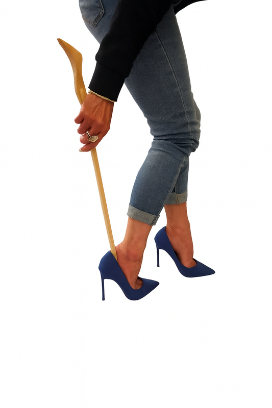 Kobieta w dżinsach i czarnym swetrze zakłada niebieskie szpilki przy pomocy drewnianej łyżki do butów – zdjęcie produktowe na białym tle, Chłopcy z Rancza / Ranch Boys.