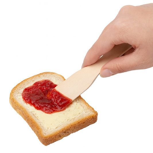 Kobieca ręka smaruje kromkę chleba masłem i dżemem truskawkowym za pomocą mini drewnianej łopatki 12 cm z bukowego drewna – zdjęcie produktowe na białym tle. Chłopcy z Rancza / Ranch Boys