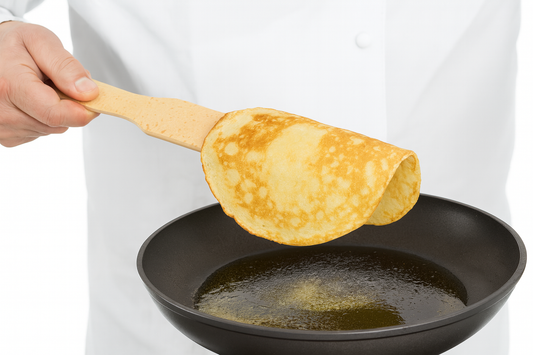 Kucharz trzyma drewnianą łopatkę o długości 24,5 cm i szerokości 4,5 cm, na której spoczywa naleśnik zwisający po obu stronach. Pod spodem znajduje się patelnia z rozpuszczonym masłem. – Chłopcy z Rancza / Ranch Boys