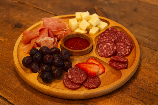 Drewniana deska obrotowa do serwowania przekąsek – elegancka, podzielona na sekcje na sery, wędliny i owoce, z małą miseczką na sos pośrodku, ustawiona na rustykalnym stole. – Chłopcy z Rancza