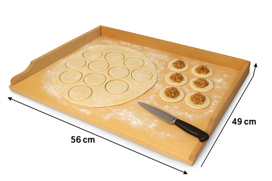 Drewniana stolnica do pierogów o wymiarach 56 × 49 cm, lekko oprószona mąką. Na lewej stronie rozwałkowane ciasto z wyciętymi krążkami, a po prawej krążki z farszem gotowe do lepienia pierogów. Na przodzie stolnicy leży nóż kuchenny. Produkt marki Chłopcy z Rancza.