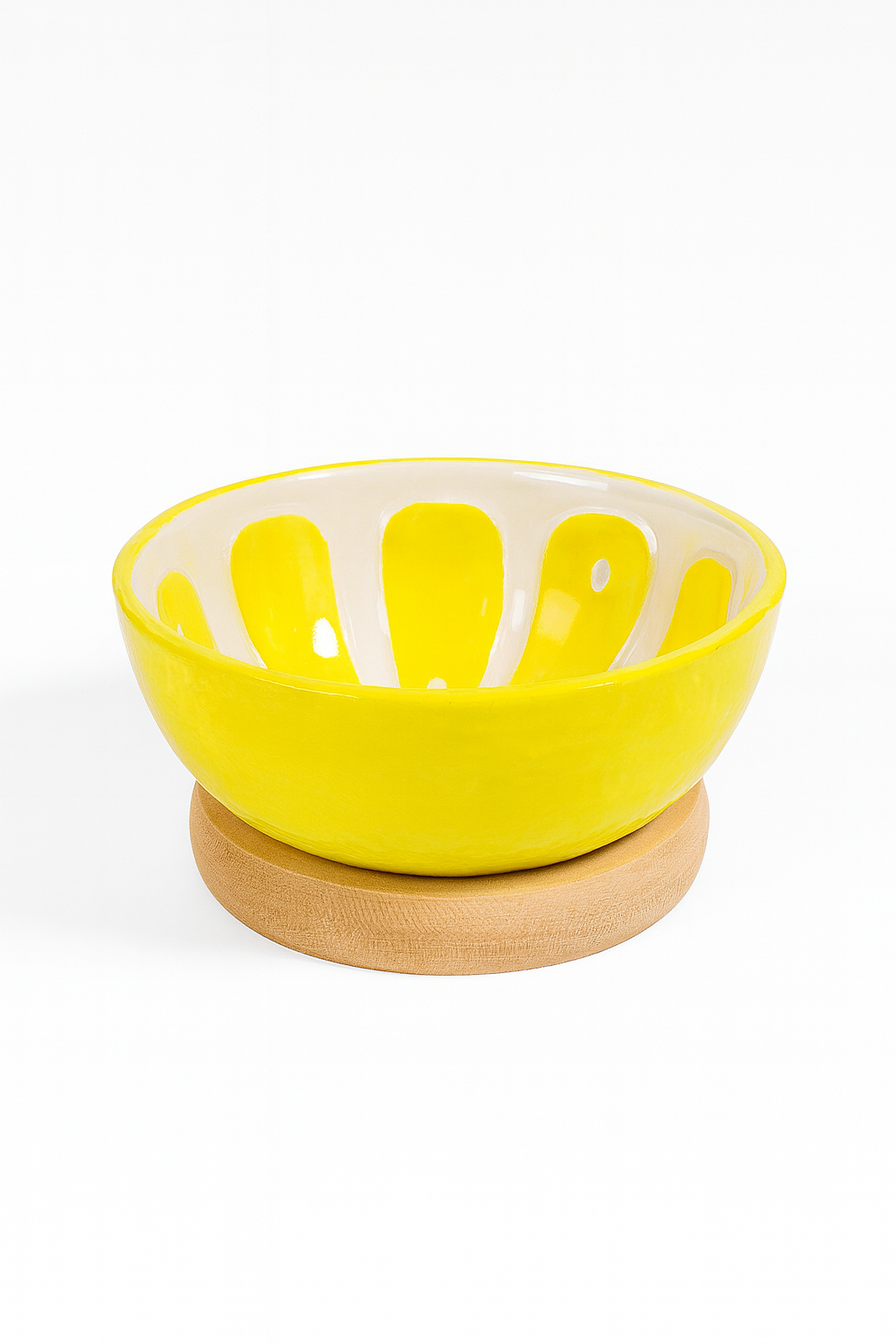 ółta ceramiczna miseczka o błyszczącej powierzchni z białymi promienistymi wzorami wewnątrz, ustawiona na okrągłej drewnianej podstawce na białym tle – elegancka dekoracja stołu i praktyczne naczynie do serwowania