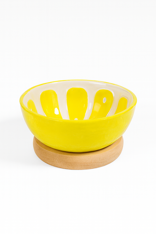 ółta ceramiczna miseczka o błyszczącej powierzchni z białymi promienistymi wzorami wewnątrz, ustawiona na okrągłej drewnianej podstawce na białym tle – elegancka dekoracja stołu i praktyczne naczynie do serwowania