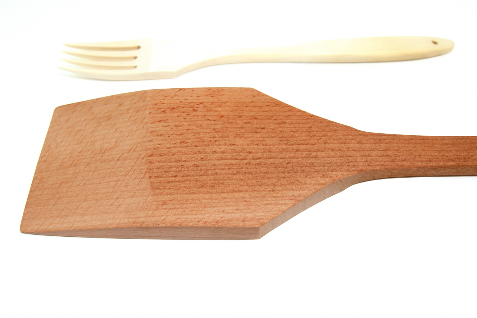 Zbliżenie na solidną drewnianą warzechę z ciemniejszego drewna bukowego oraz jasny widelec kuchenny leżący w tle. Oba narzędzia są wykonane z naturalnego drewna i zaprezentowane na białym tle – Chłopcy z Rancza / Ranch Boys.