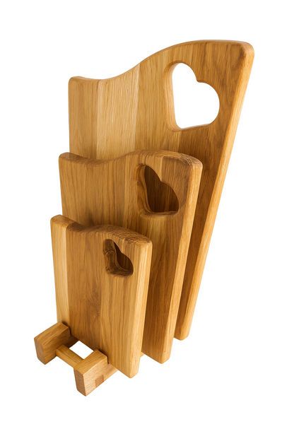 Komplet trzech dębowych desek kuchennych z otworami w kształcie serca, ustawionych na eleganckiej drewnianej podstawce. Deski wykonane z naturalnego, olejowanego dębu w ciepłym odcieniu – idealne do serwowania i krojenia w nowoczesnej kuchni.