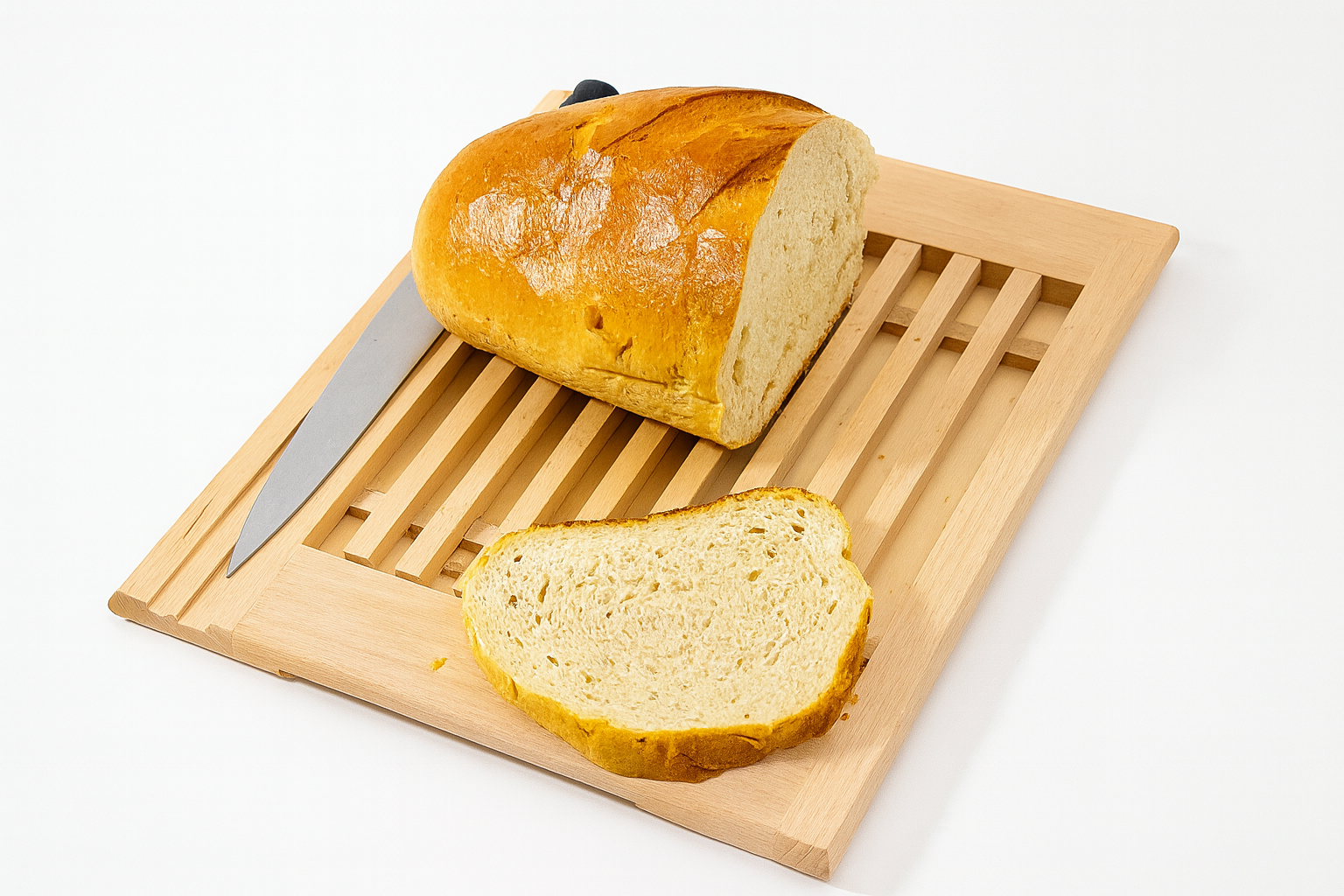 Drewniana deska do krojenia z rusztem na okruchy, wykonana z jasnego drewna bukowego. Na desce leży nóż do chleba oraz bochenek świeżego, chrupiącego chleba z odkrojonym plastrem.