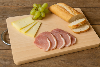 Duża prostokątna deska bukowa o wymiarach 25×35 cm i grubości 1,5 cm z metalowym uchwytem. Na desce ułożone są plasterki sera, winogrona, kilka kromek bagietki i kawałki mięsa. Całość na rustykalnym stole z naturalnego drewna, w ciepłym świetle dziennym.
